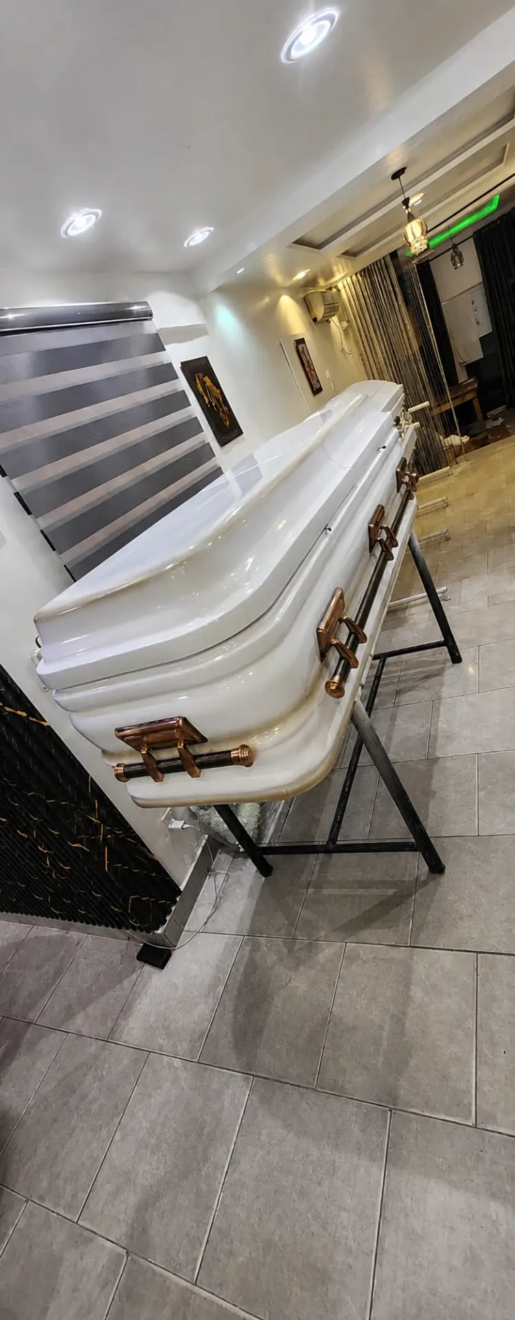 Pearl white casket with copper rose gold handles displayed on a black trestle stand