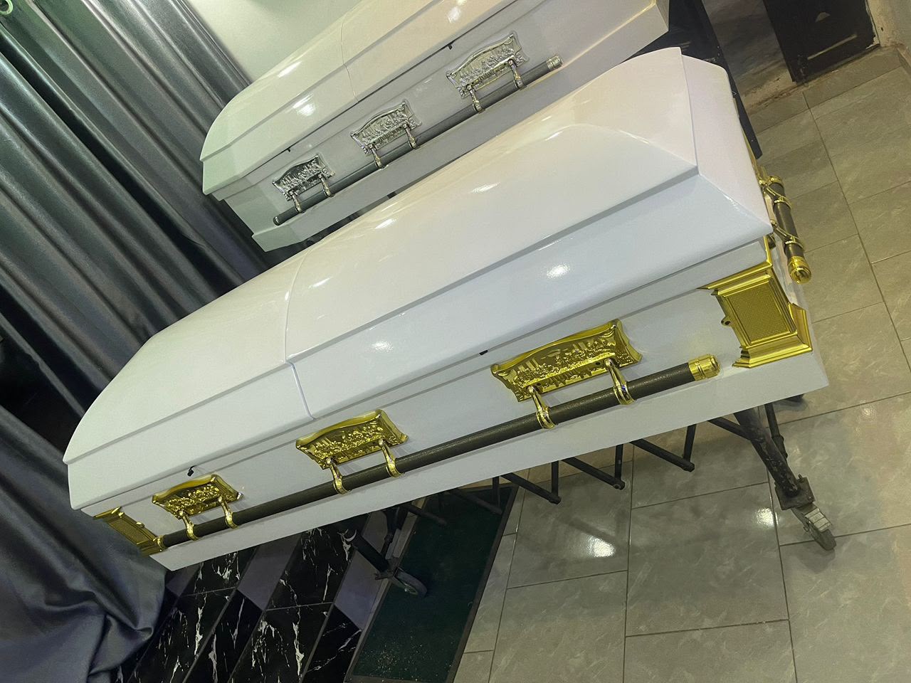 White gloss casket with polished gold swing handles on a stand