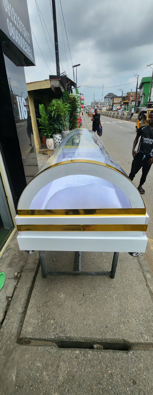 White casket with gold-tone trim on a wheeled stand outdoors
