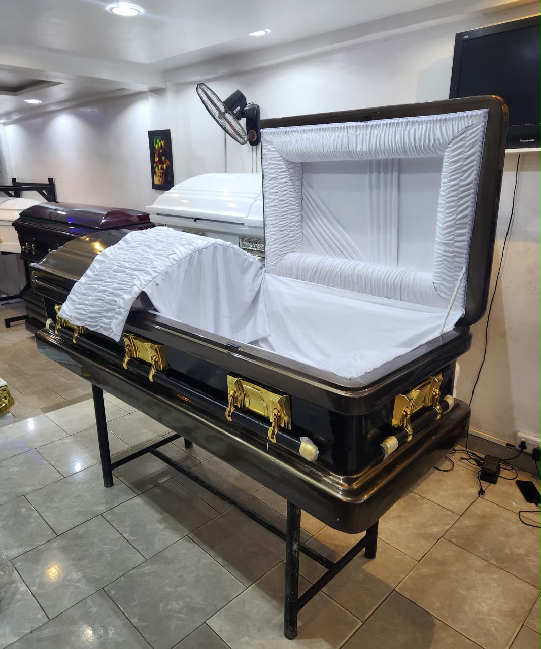 Open black casket with a white ruched interior and gold-tone fittings in the showroom