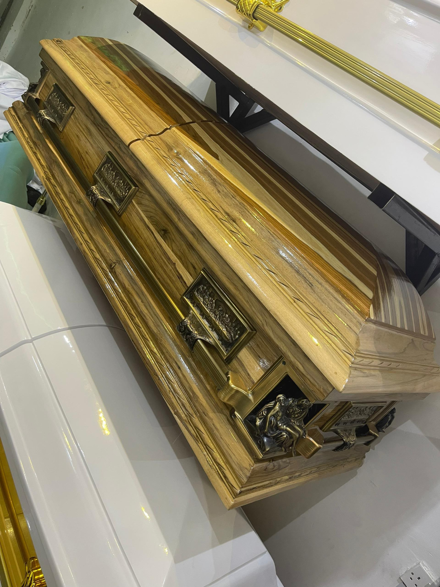 Golden wood-finish casket with ornate dark metal handles