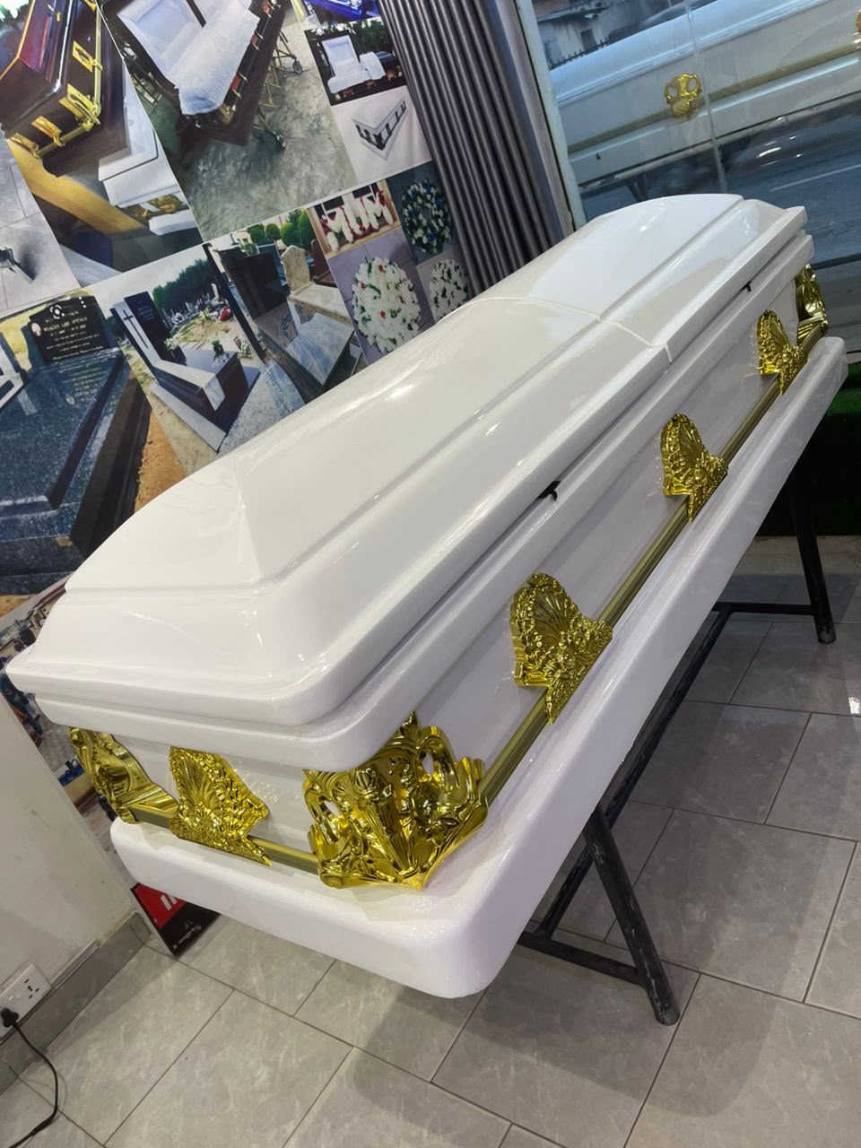 Gloss white casket with a domed lid and ornate gold handles on a display stand