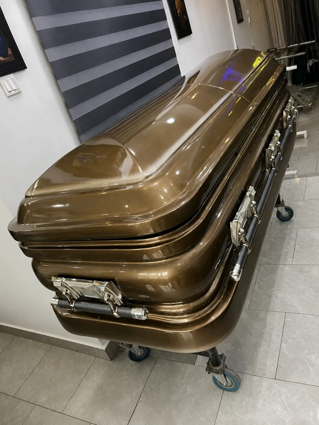 Metallic bronze executive casket with chrome swing-bar handles on a rolling church truck