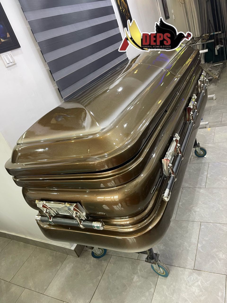 High-gloss metallic bronze casket with chrome handles and dark swing bars on a trolley